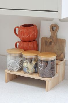 there are three jars and two mugs on the shelf next to each other, one is filled with coffee beans