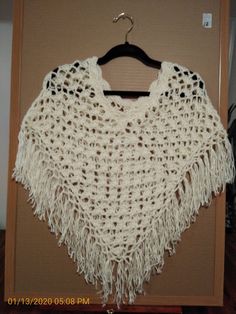 a white crocheted shawl hanging on a wooden hanger in front of a wall