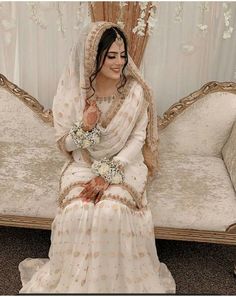 a woman sitting on top of a couch wearing a white dress and holding a bouquet