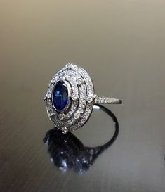 DeKara Designs Collection Art Deco Inspired Extremely Elegant Halo Sapphire Diamond Engagement Ring. Metal- 90% Platinum, 10% Iridium. Stones- 1 Oval Ceylon Blue Sapphire 1.25 Carats, 100 Round Diamonds F-G Color VS2 Clarity .80 Carats. Size- 6 1/4. An Amazing Art Deco Inspired Ceylon Blue Sapphire Triple Halo Diamond Engagement. The ring features a beautiful Ceylon Blue Sapphire that is expertly bezel set in the center. The sapphire is surrounded by 92 pave and burnish set round sparkling diamo Luxury Oval Diamond Cut Sapphire Ring, Luxury Sapphire Diamond Ring With Polished Finish, Hallmarked Platinum Cluster Ring, Luxury Sapphire Diamond Ring In 14k White Gold, Platinum Rings With Baguette Cut Gemstone, Platinum Baguette Cut Gemstone Ring, Baguette Cut Platinum Gemstone Rings, Luxury Sapphire Platinum Rings, Exquisite Platinum Hallmarked Diamond Ring