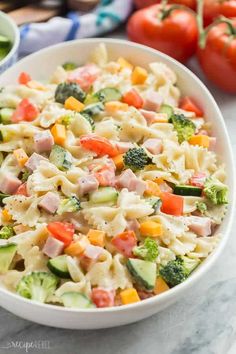 a white bowl filled with pasta salad next to tomatoes and broccoli on a table