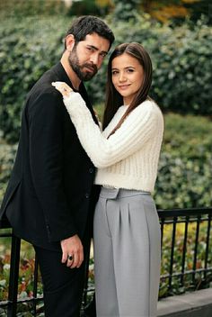 a man and woman standing next to each other in front of a black iron fence