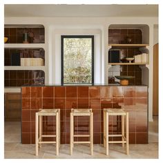 two wooden stools sitting in front of a kitchen counter with brown tiles on it