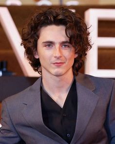 a man with curly hair wearing a gray suit and black shirt