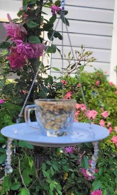 a bird feeder hanging from the side of a house with pink flowers in the background