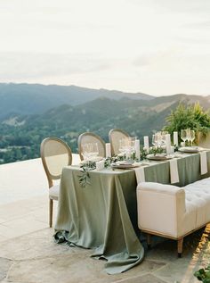 a table set up with place settings and greenery on it for an outdoor dinner