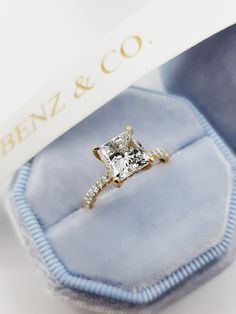 an engagement ring with a princess cut diamond set in yellow gold and diamonds on the band