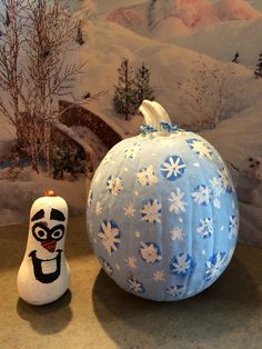 a blue and white painted pumpkin sitting next to a snowman figurine on a table