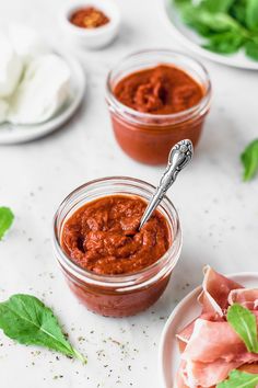 small jars filled with tomato sauce and garnished with basil leaves on the side