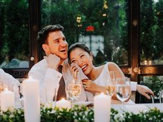 a man and woman sitting at a table with wine glasses in front of them, surrounded by candles