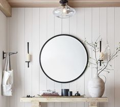 a round mirror hanging on the wall next to a table with vases and candles