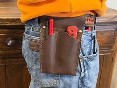 a person wearing a brown leather belt with red pens and pencils in their pocket