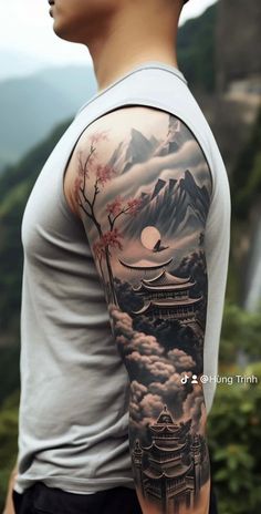 a man with a tattoo on his arm is standing in front of mountains and clouds