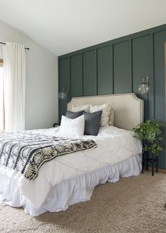 a bedroom with green paneled walls and a white bed in the center, along with two planters on either side of the bed