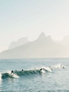 several surfers are riding the waves in the ocean with mountains in the back ground