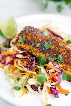 a white plate topped with fish, coleslaw and lime wedges next to a slice of lime