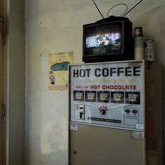 a hot coffee vending machine in front of a tv set on top of it