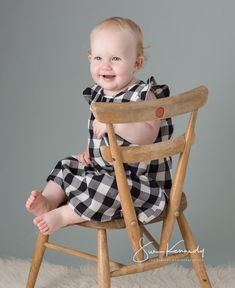 a baby sitting in a wooden chair on top of a white rug and smiling at the camera