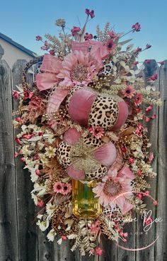 a wreath with pink flowers, leopard print and other things hanging on a wooden fence