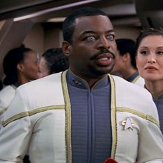 two people standing next to each other in front of a group of others wearing star trek uniforms