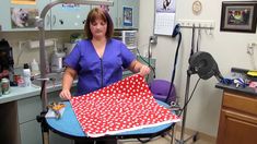 a woman in a blue shirt is holding a red and white polka dot fabric on a sewing machine