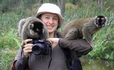 a woman is holding two monkeys on her shoulder and taking a photo with a camera