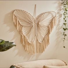 a butterfly shaped wall hanging on the side of a white wall next to a plant