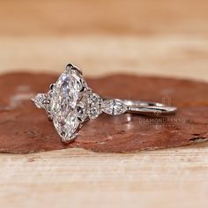 a diamond engagement ring sitting on top of a piece of wood with leaves around it