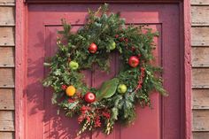 a christmas wreath hanging on the front door of a red building with greenery and fruit