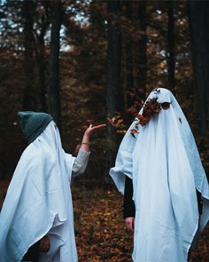 two people dressed in white are walking through the woods with their hands out to each other