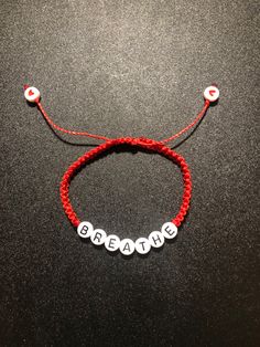 a red string bracelet with white beads and the word breathe written in small letters on it