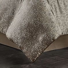 a bed covered in a silver blanket on top of a wooden floor