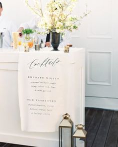 two chefs preparing food at a white bar with flowers in vases on the counter