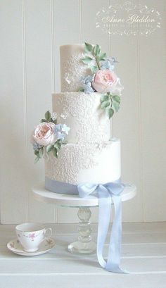 a white wedding cake with pink roses and blue flowers on top is sitting on a table