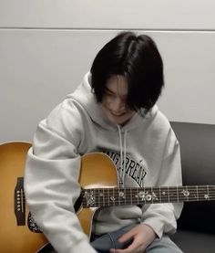 a person sitting on a couch with a guitar in front of them and wearing a hoodie