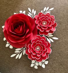 three paper flowers on the ground with leaves and stems attached to each flower, all in red