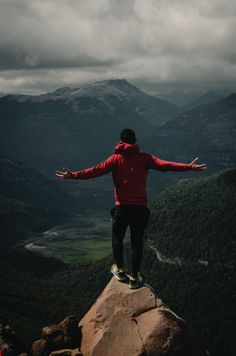 a man standing on top of a rock with his arms wide open in the mountains