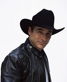 a man wearing a black cowboy hat and leather jacket with his hands in his pockets