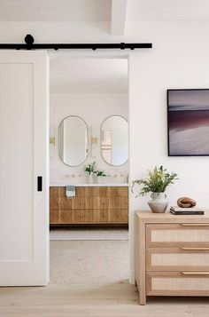 an open door leading to a bathroom with two mirrors on the wall and a wooden dresser