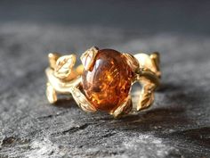 a gold ring with an orange stone in the center on top of a black surface