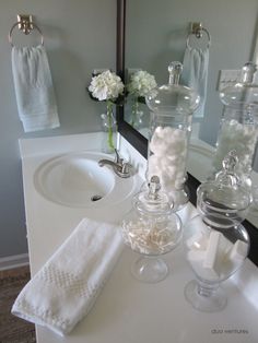 a bathroom sink with two clear glass vases on top of it next to a white towel