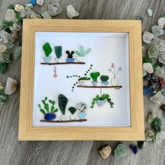 a shadow frame with sea glass and rocks in it on a table next to stones