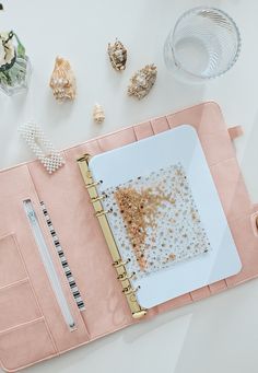 a pink notebook with gold confetti on it and some other items around it