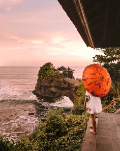 a woman holding an orange umbrella looking out at the ocean