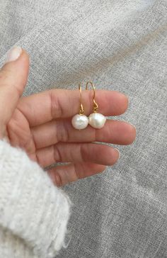 a person holding two small white pearls in their hand and wearing gold ear wires on top of them