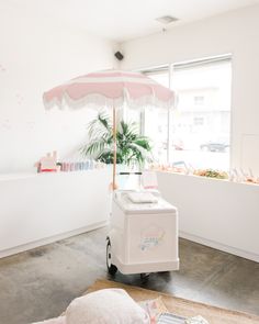 an ice cream cart in the corner of a room with a pink umbrella over it