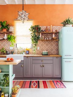 a kitchen with an orange wall and lots of potted plants