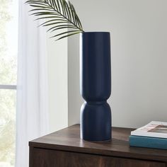 a blue vase sitting on top of a wooden table next to a book and plant