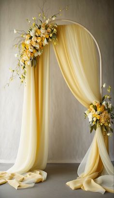 a yellow and white wedding arch with flowers on the top, draped over by draping