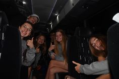 a group of young people sitting in the back of a bus giving thumbs up signs